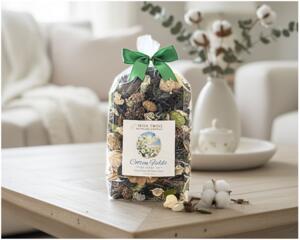 Irish Twins 'Cotton Fields' potpourri on wooden table. Cozy living room background with white sofa and cotton flowers. Fresh home fragrance.